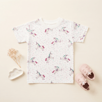 White baby t-shirt with unicorn pattern laid flat, styled with dried flowers and a cloud-shaped trinket dish on a cream background